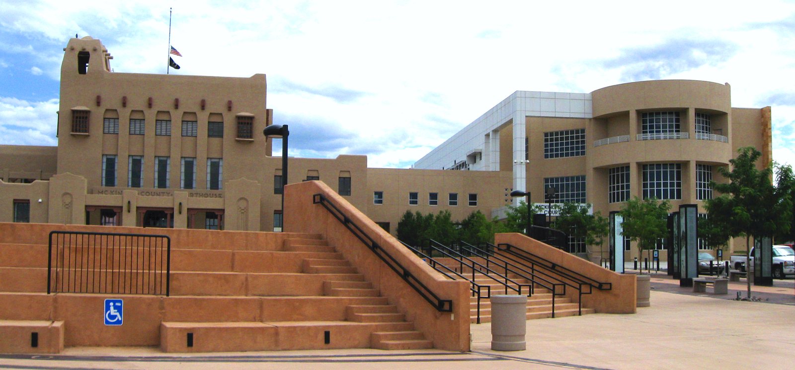 The tan, flat-roofed McKinley County Courthouse in Gallup, New Mexico, with wide plaza steps in front, under a blue sky with white clouds